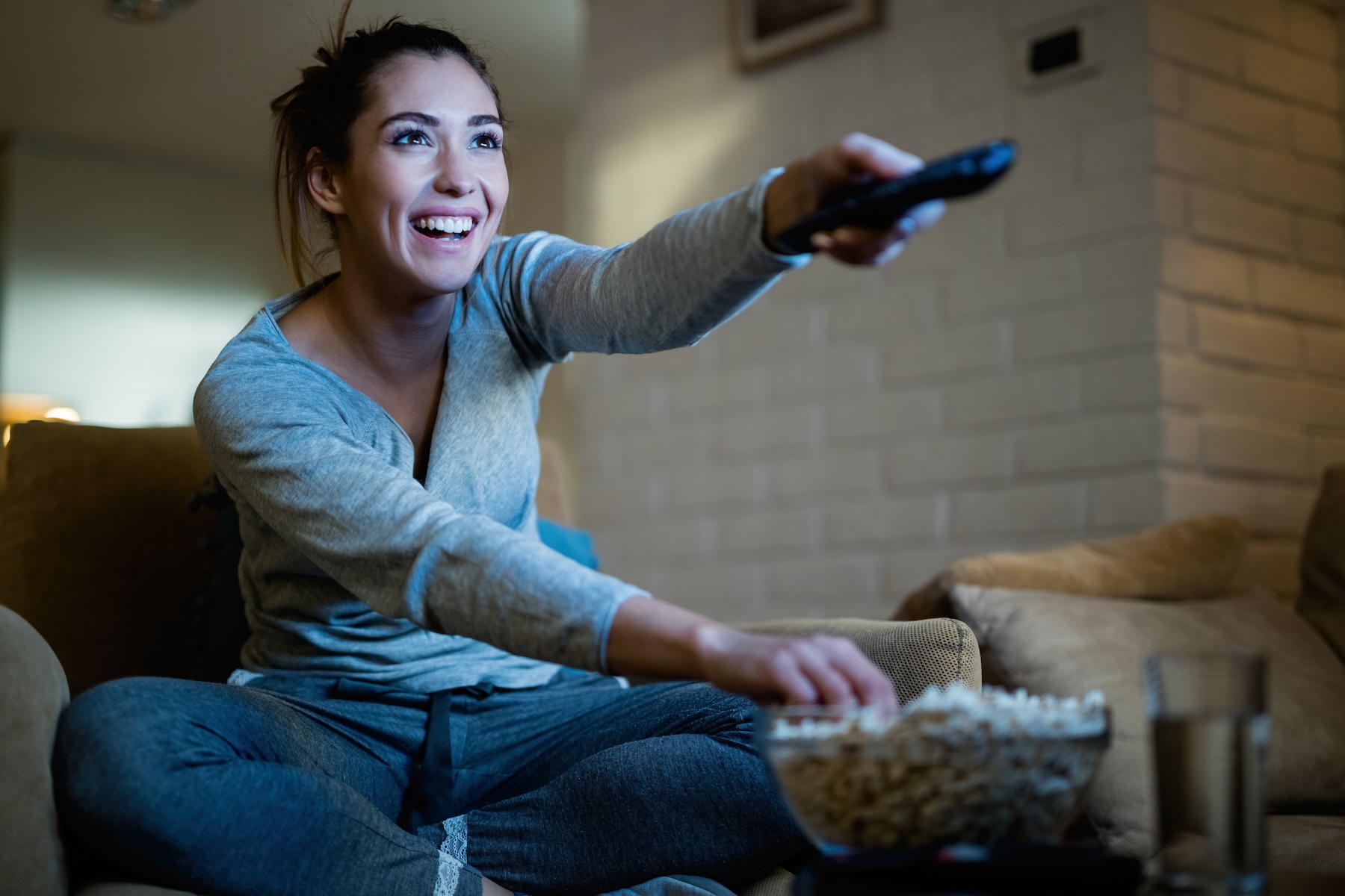 Young happy woman changing TV channels with remote control